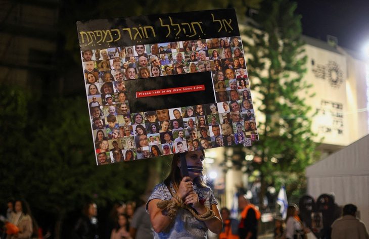 Một người biểu tình cầm tấm biển in hình các con tin bị Hamas bắt cóc ở Tel Aviv, Israel, ngày 2-12 - Ảnh: REUTERS